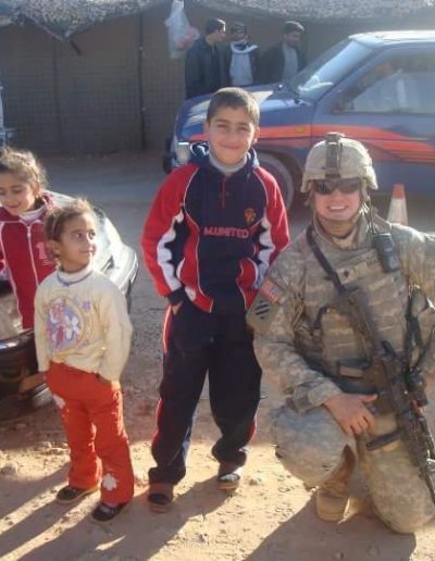 A soldier kneels next to two children and holding an ar-1 5.