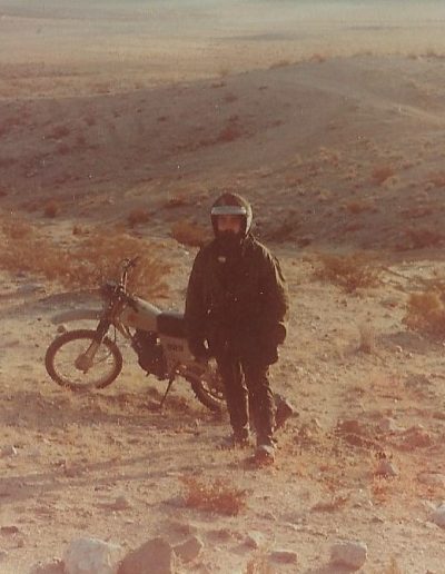 A man standing in the desert with his motorcycle.