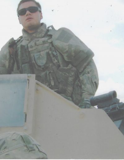 A soldier standing on top of an armored vehicle.